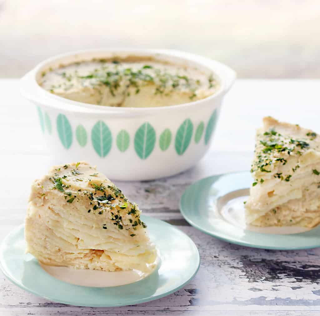 Vegan scalloped potatoes in a retro white and blue pyrex dish and portions on 2 blue and whit plates.