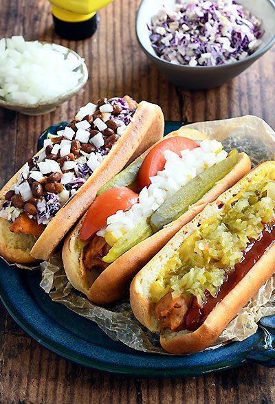 3 gluten free vegan hot dogs in gluten free buns with various toppings