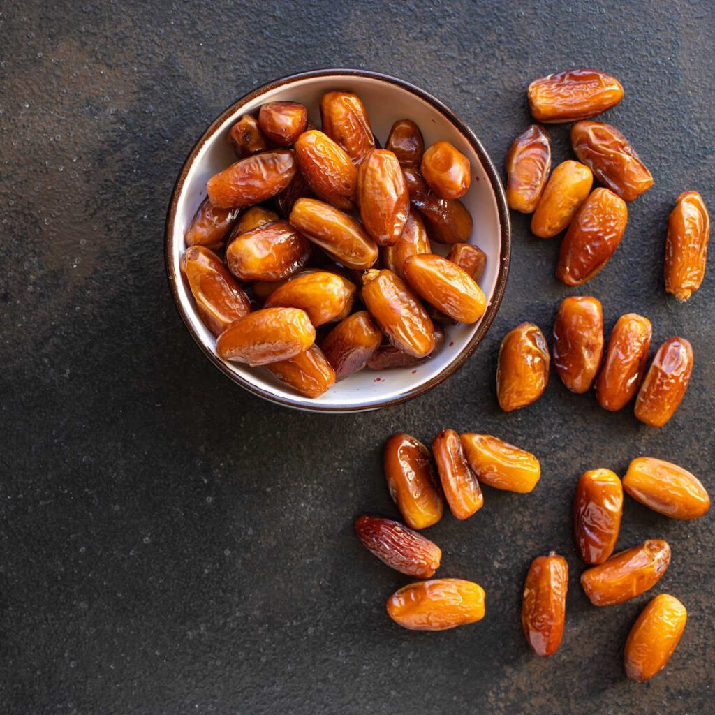 Dates in a metal bowl on a dark cement table.