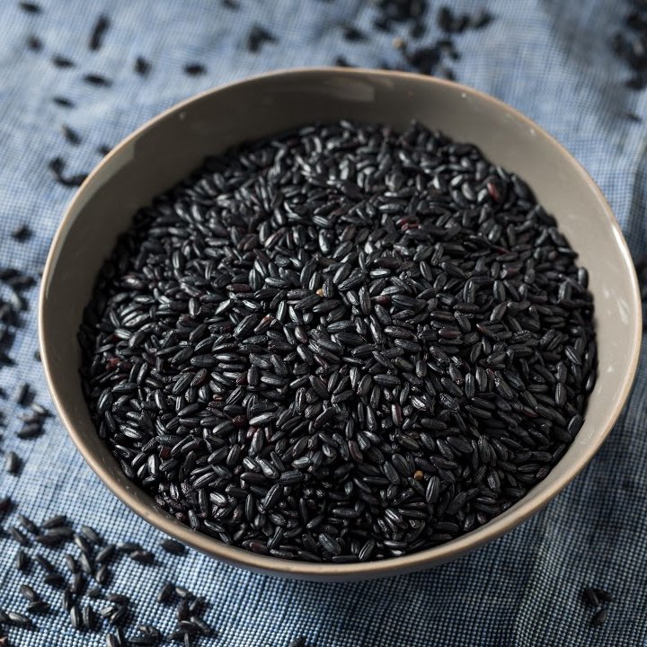 Black forbidden rice in a tan bowl on a blue cloth placemat.