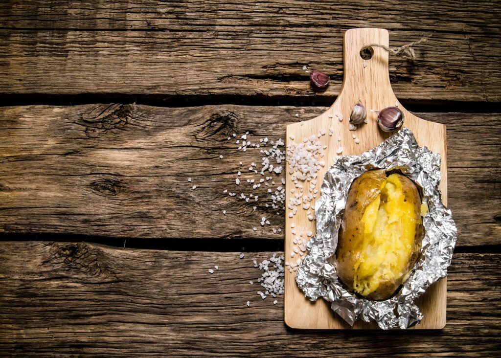 Potato baked in foil on a wooden cutting board.